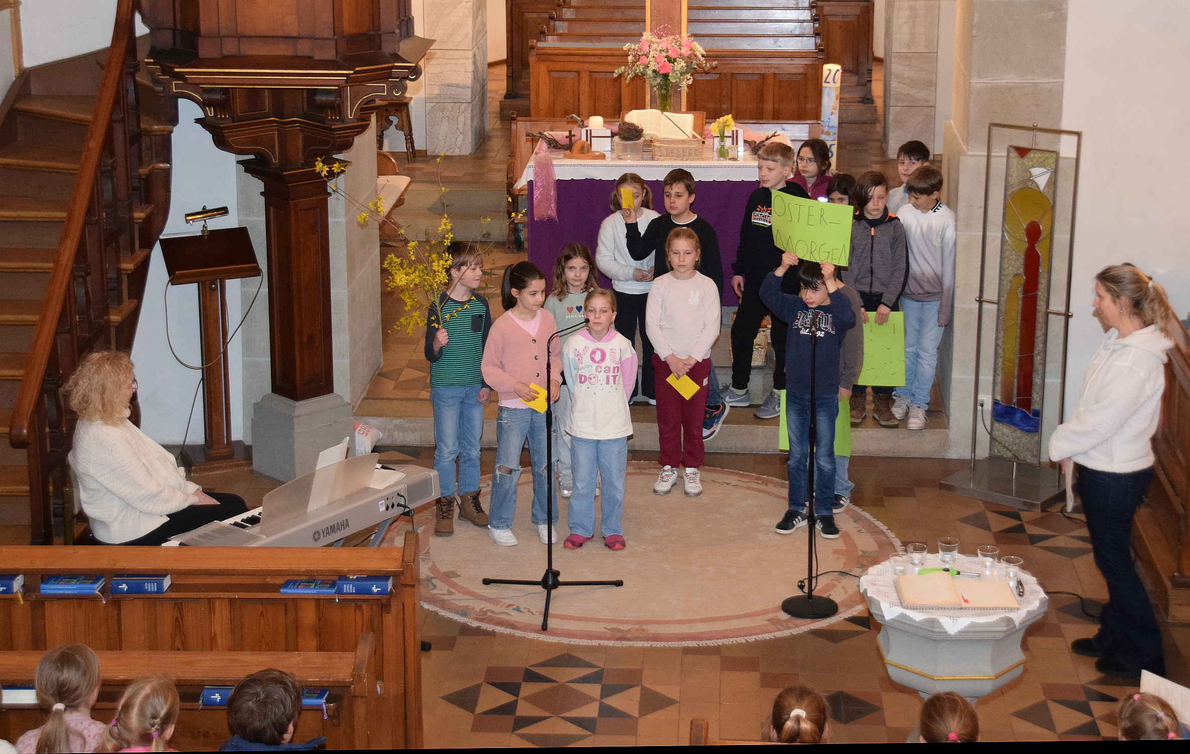Foto mit Kindern vor dem Altar, ein Kind hält ein Schild hoch mit der Aufschrift Ostermorgen